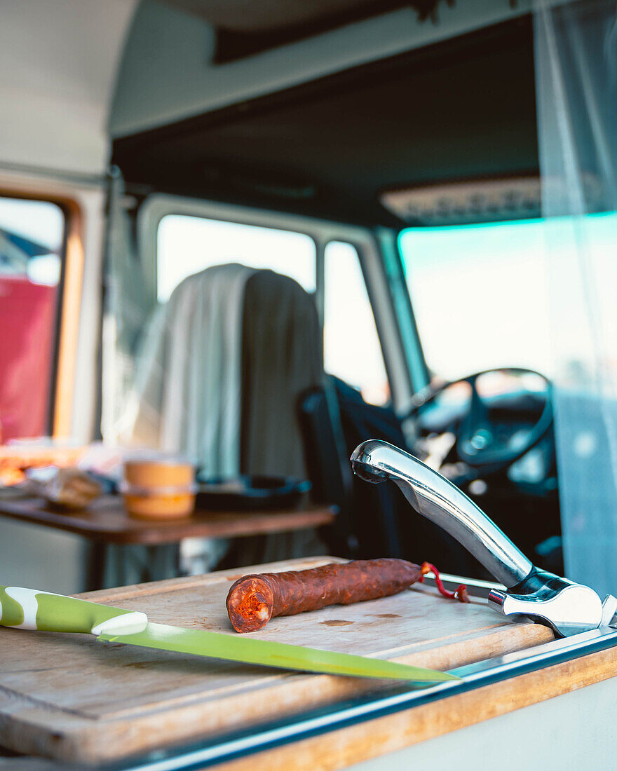 Cured smoked chorizo sausage near knife on wooden chopping board in trailer during vacation in Cantabria