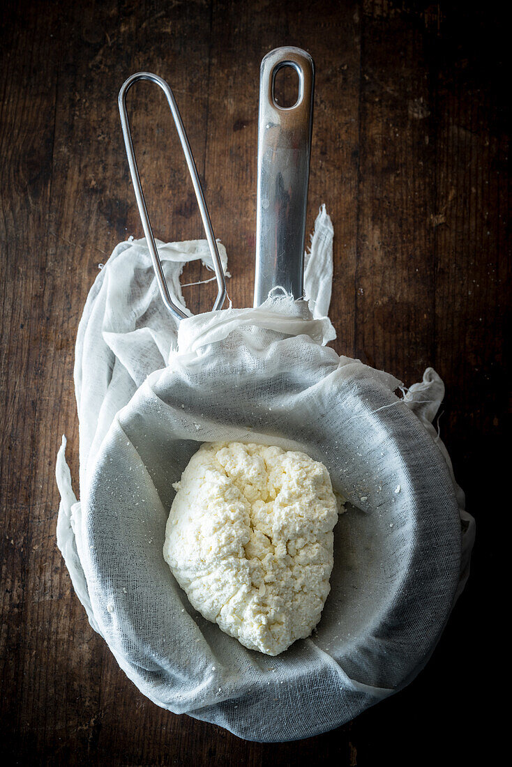 Top view of fresh homemade cottage cheese in colander with cloth placed on wooden table
