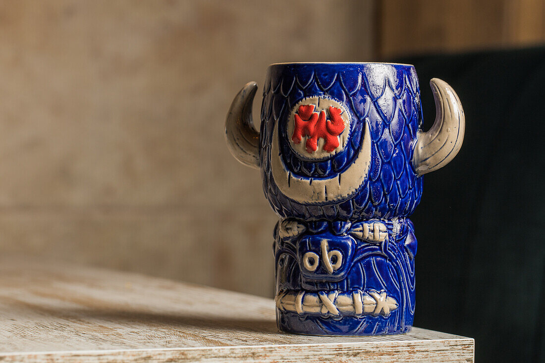 Bull shaped tiki mug of alcohol drink with froth placed against wooden table on blurred background