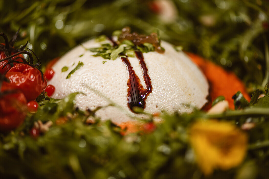 Close up view of yummy burrata cheese on cold tomato cream with arugula leaves and cherry tomatoes with truffles and peanuts