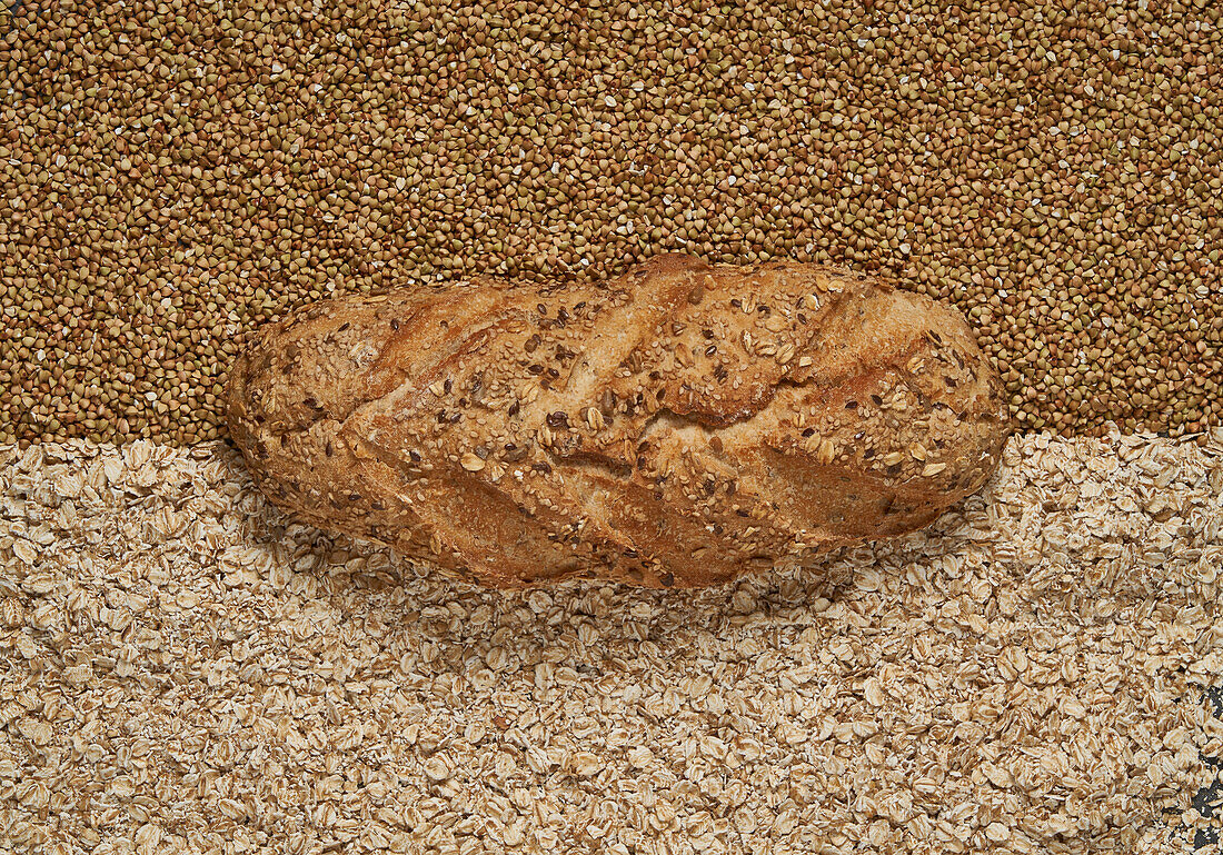 Top view full frame of freshly baked buckwheat and oat loaf of bread placed on raw grains in light room
