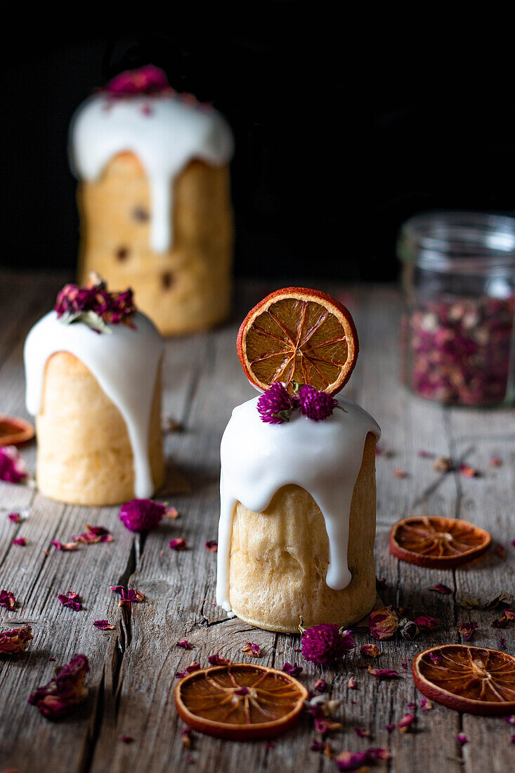 Several delicious homemade kulichs poured with sweet glaze and decorated with pieces of dry orange and flowers on wooden table