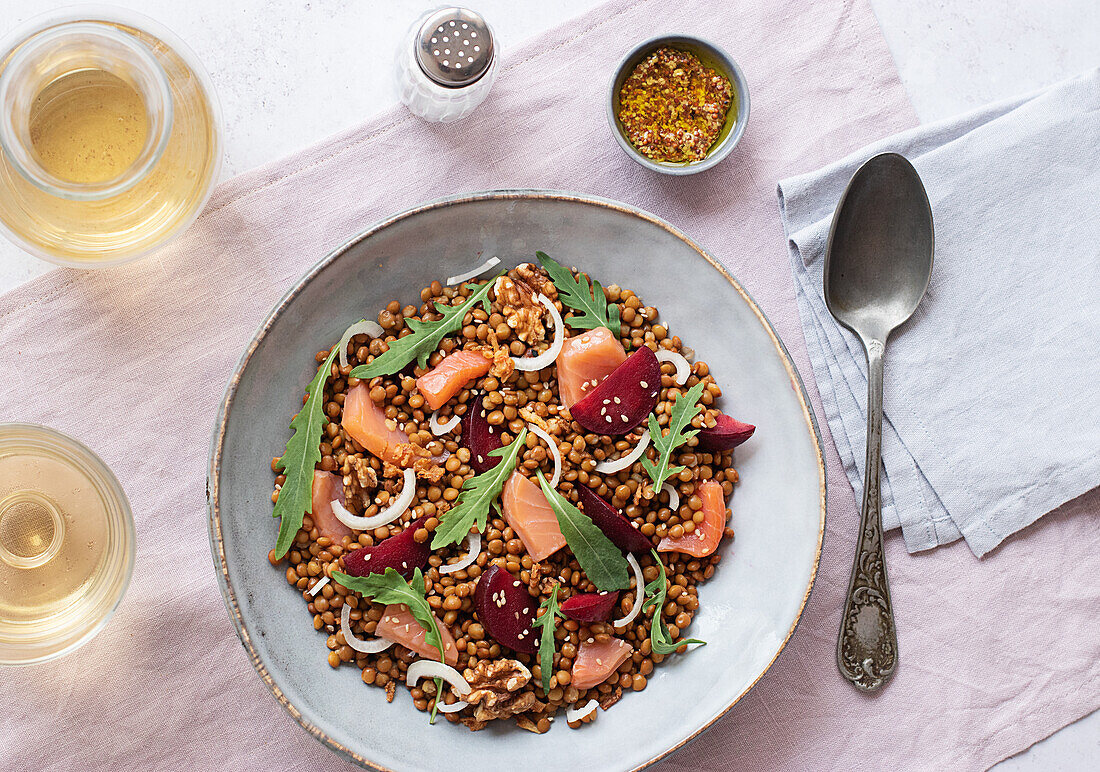 Closeup of a salmon and lentil salad seen from above on a table with a pink tablecloth