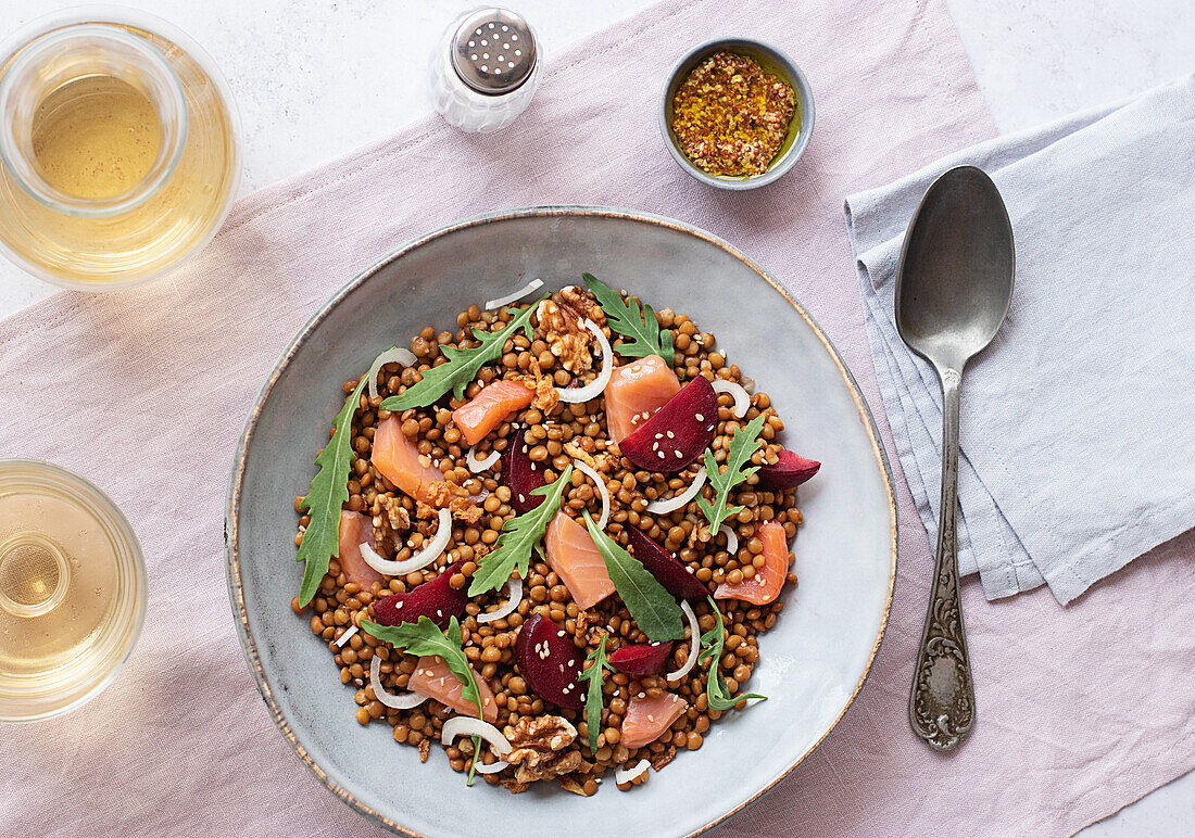 Nahaufnahme eines Lachs- und Linsensalats von oben auf einem Tisch mit rosa Tischtuch