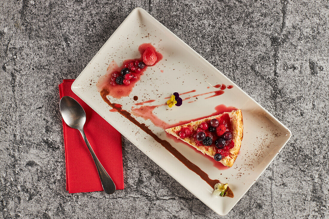 Blick von oben auf ein Stück köstlichen Käsekuchens mit roten Beeren und Marmelade, serviert auf einem rechteckigen Teller in der Nähe von Wassergläsern in einem Restaurant