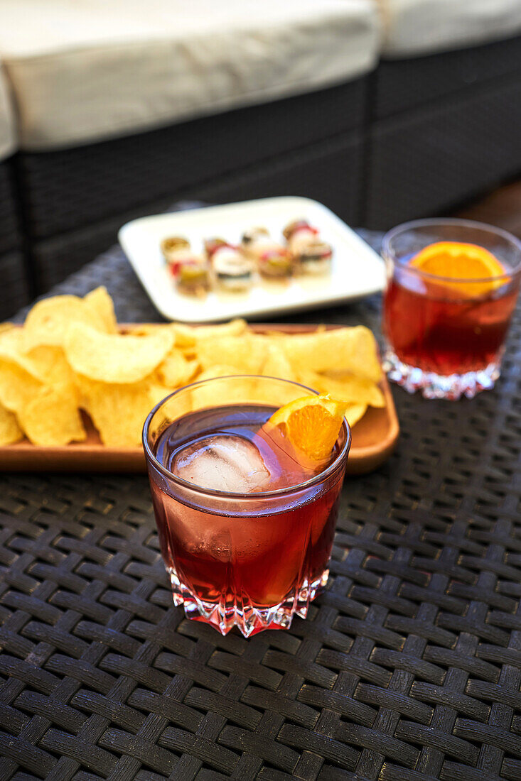 From above of glass with cold old fashioned cocktail with ice and orange slice served on table with appetizers