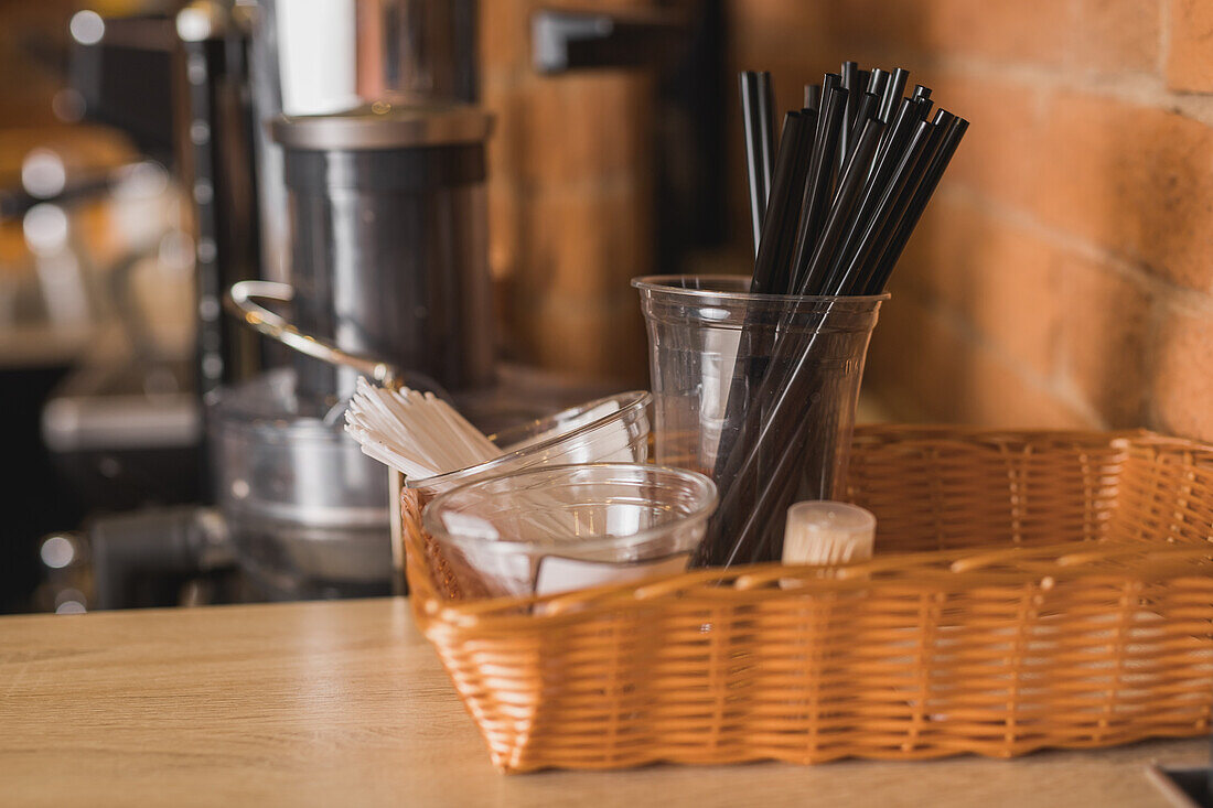 Entsorgungsstrohhalme für Kaffee mit Rührstäbchen, Zucker und Zahnstochern in einem Korb auf dem Tresen eines Cafés