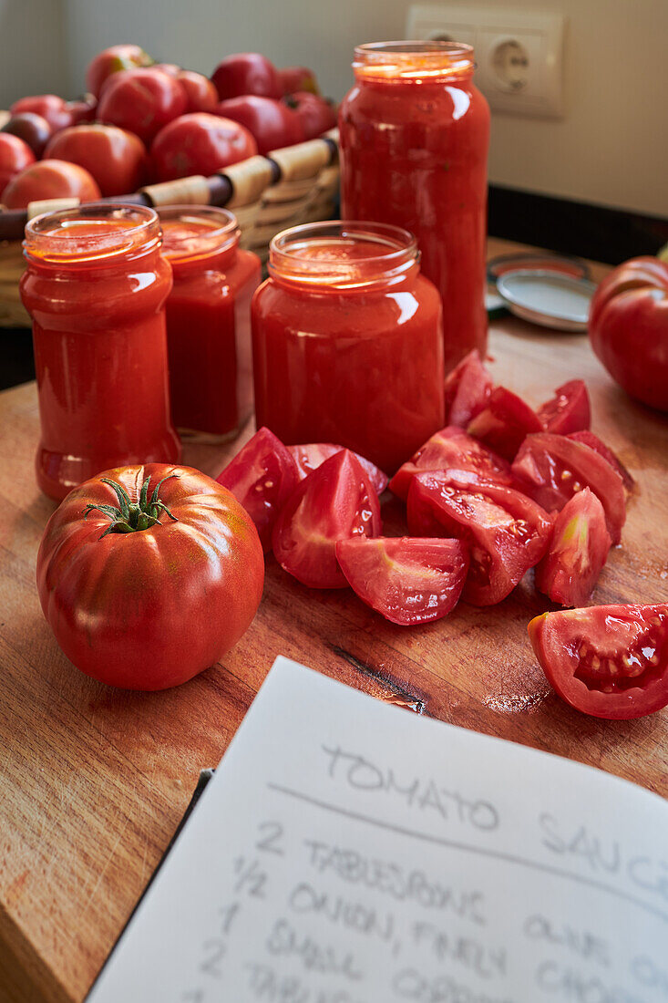 Reife rote Tomaten und Gläser mit Soße stehen auf dem Tisch neben einem Notizbuch mit Rezept in der Küche