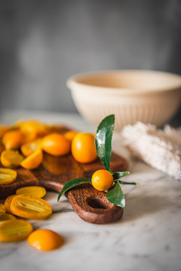 Pile of fresh orange cut kumquats on wooden chopping board placed on marble table with towel in kitchen