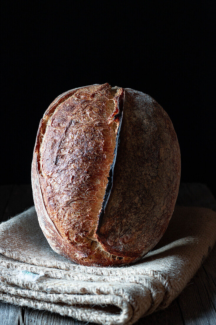 rustic homemade fresh sourdough rye loaf on blanket in black background