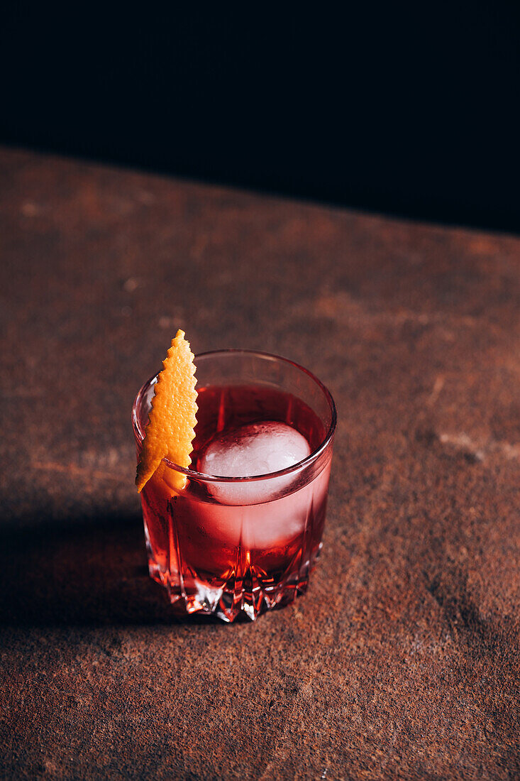 Glass of refreshing alcoholic Negroni cocktail garnished and orange peel and placed on table amidst barman tools