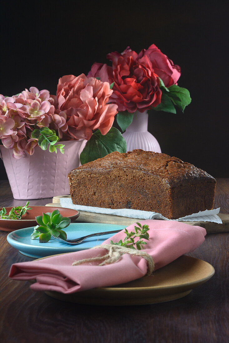 Stilleben eines Biskuittörtchens neben einigen rosa Vasen mit Blumen auf einem Tisch