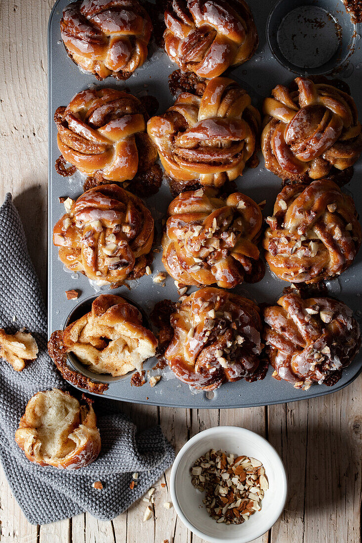 Top view pile of tasty freshly baked homemade cinnamon buns placed on wooden table with ground nuts in light kitchen