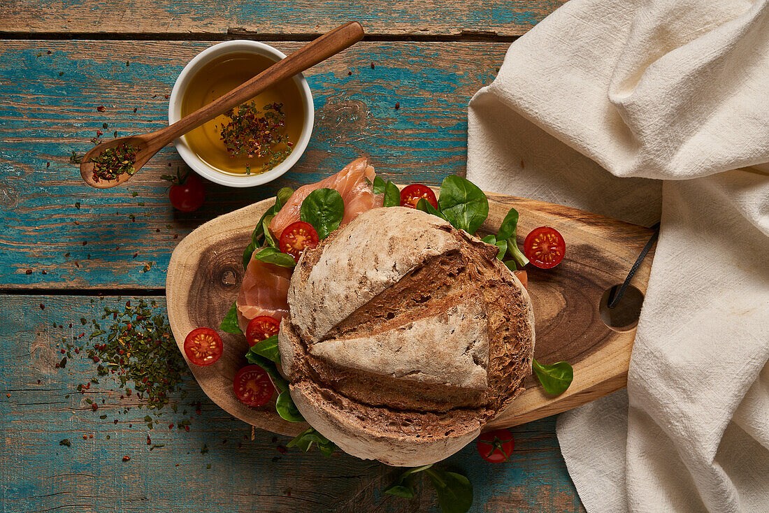 Top view of homemade sourdough bread with salmon served on wooden cutting board with cherry tomatoes on shabby table