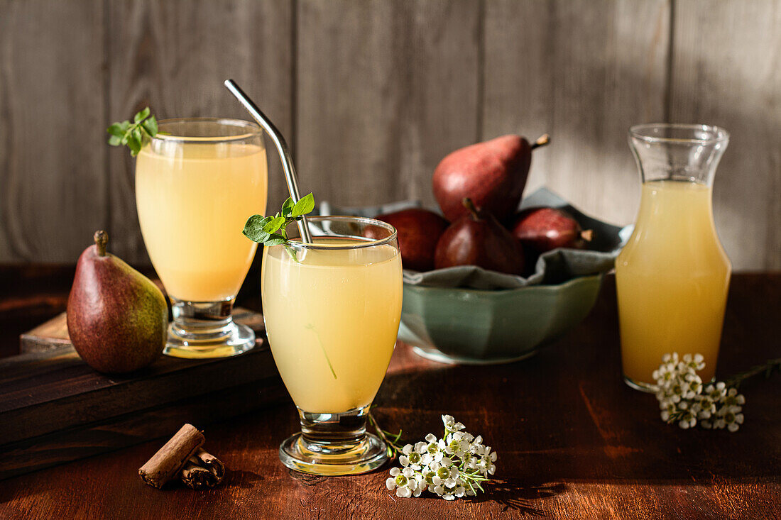 Glasses of delicious refreshing drinks with pear juice and fresh elderflower leaves on table with cinnamon sticks