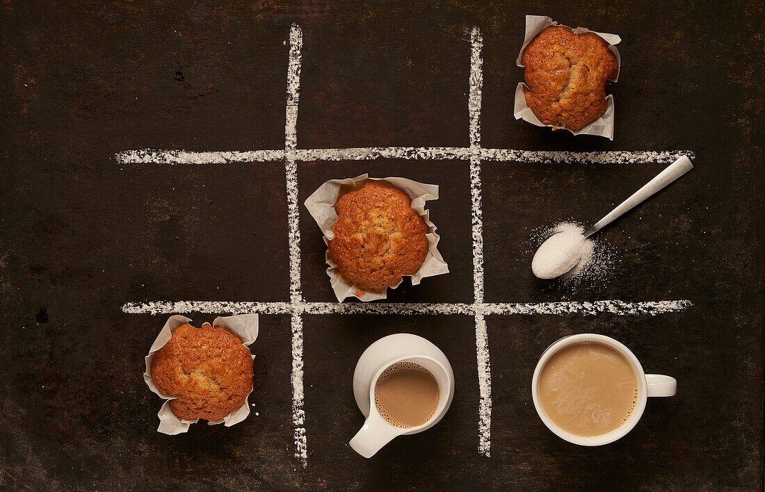 Top view of edible Tic tac toe game with baked muffins and spoon with sugar and cup of coffee with milk representing noughts and crosses placed on black background