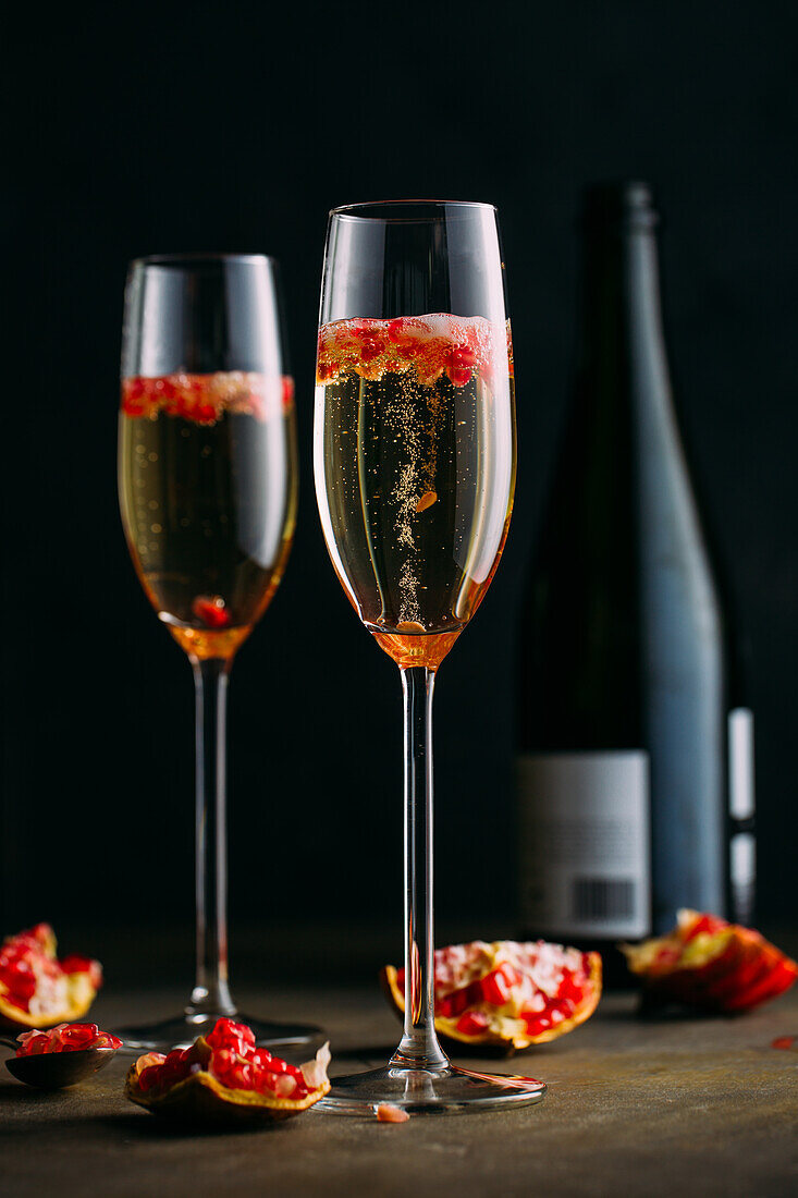 Champagner-Cocktail mit Granatapfel auf rustikaler Oberfläche vor dunklem Hintergrund