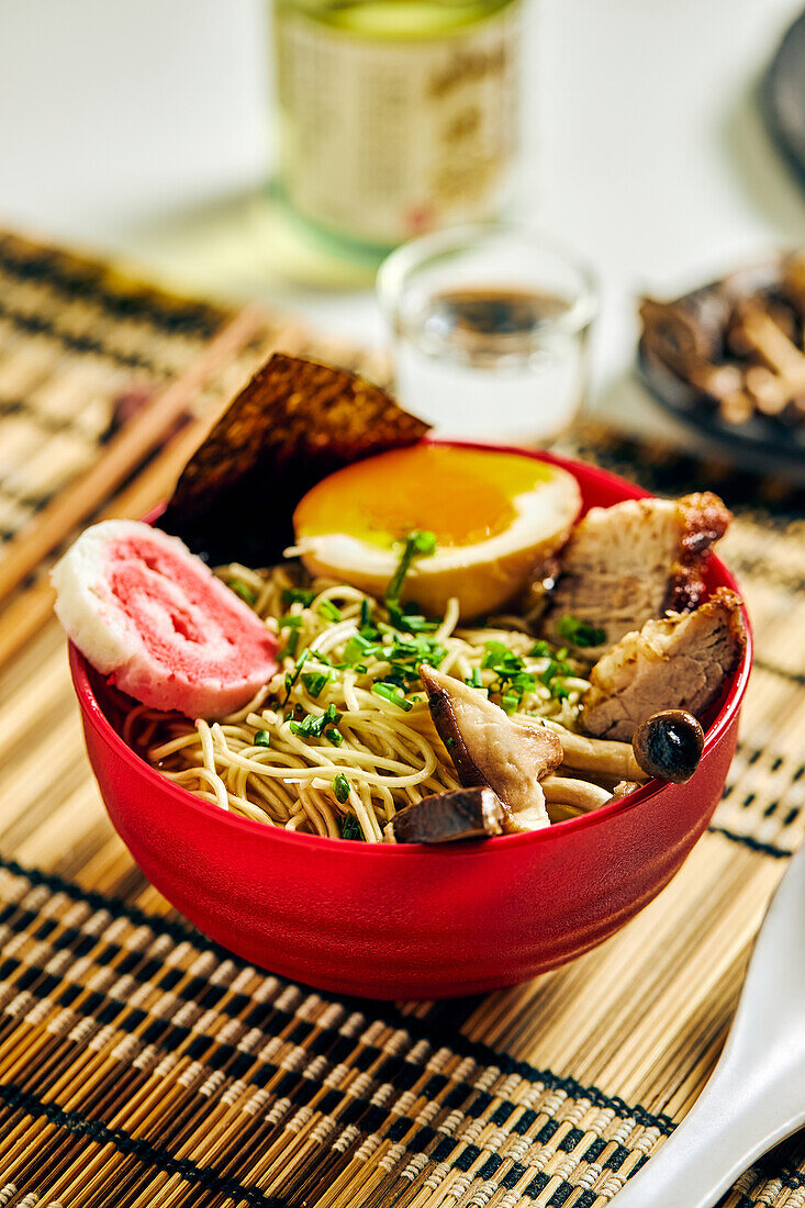 From above of appetizing ramen soup with meat and egg and noodles served in bowl on table near chopsticks and glass cup