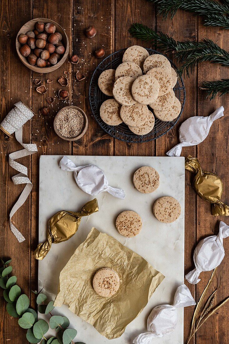 Draufsicht auf eine Reihe süßer, runder Butterkekse mit Haselnüssen, die mit Geschenkpapier und Bändern auf einem Holztisch arrangiert sind