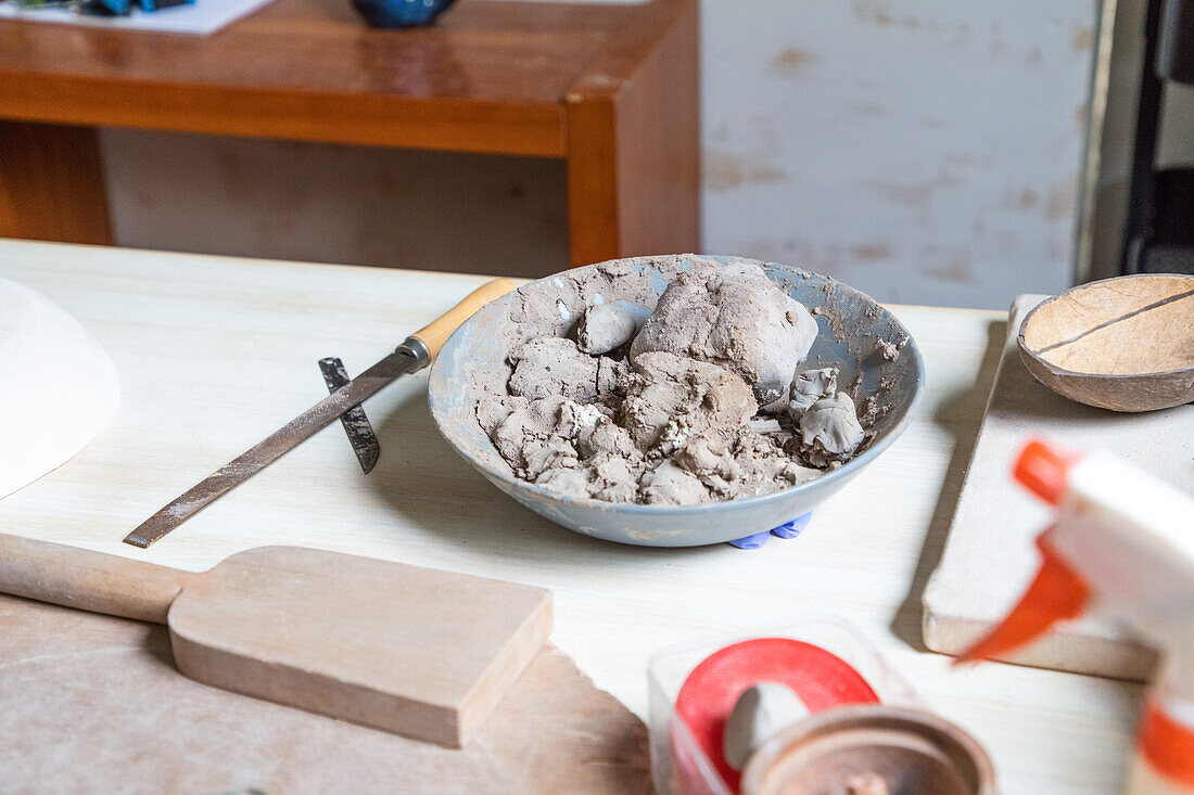 Von oben Schale mit weichem Ton auf Holztisch in der Nähe von Töpferwerkzeugen in der Werkstatt platziert