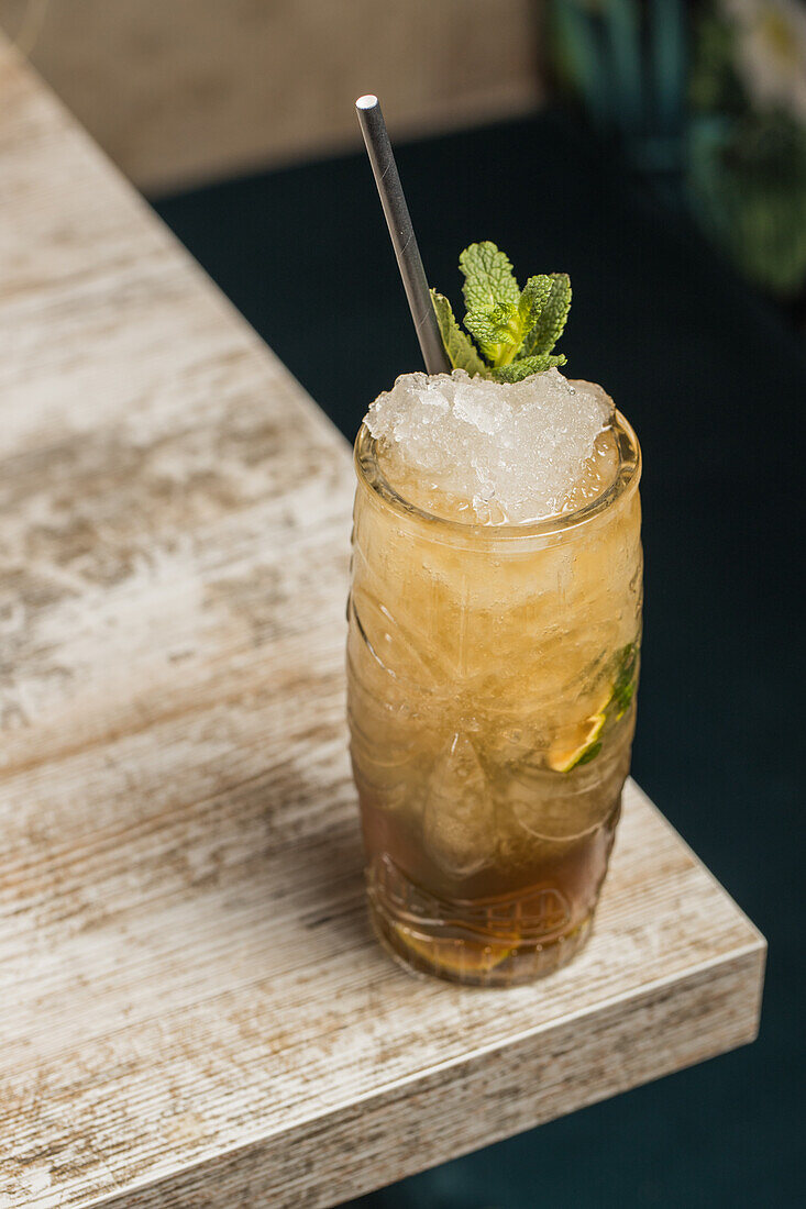 From above of tiki cup with cold alcohol drink with straw served with ice and decorated with fresh herb placed on blurred background