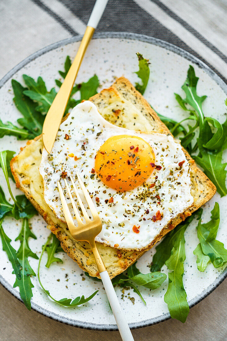 Von oben Toast mit Eiern und Käse und Rucolasalat auf einem Teller auf dem Tisch serviert