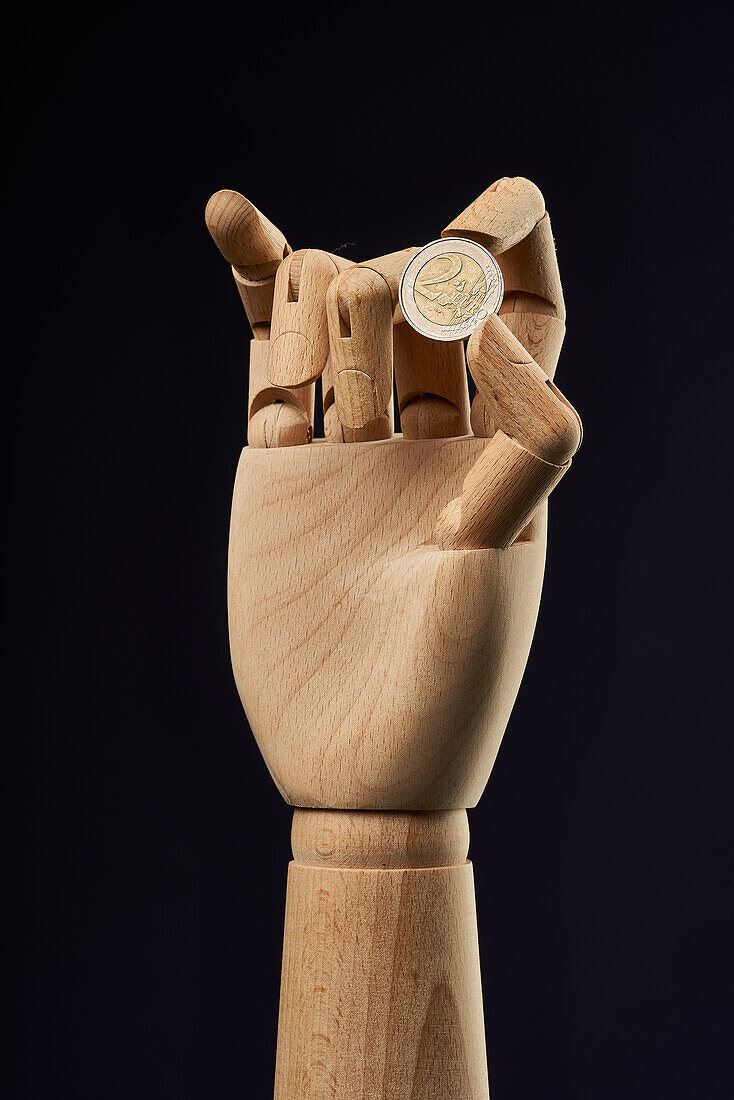2 euro coin in wooden hand on black background in studio showing concept of finance