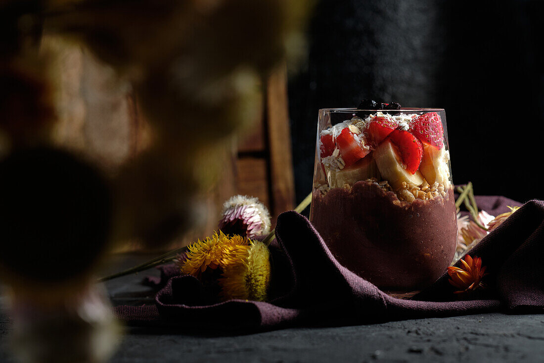 Appetizing smoothie bowl with granola strawberries and blueberries placed on table near various wildflowers