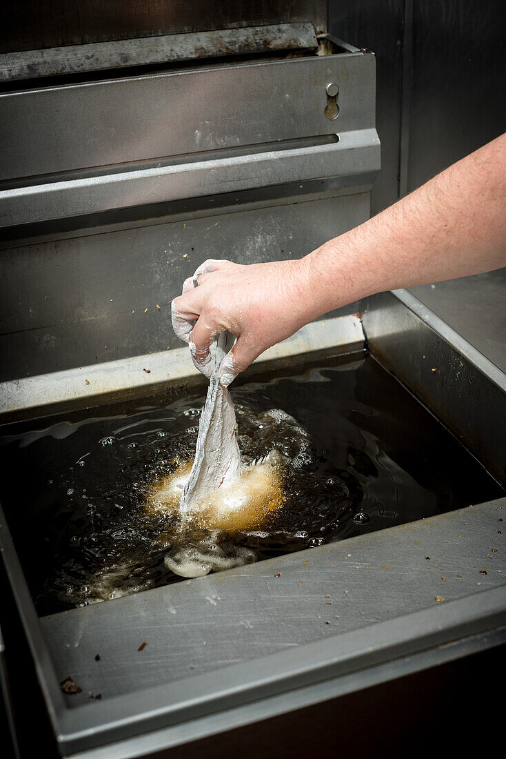 Crop unrecognizable cook preparing fish in oil in deep fryer while cooking in kitchen of restaurant