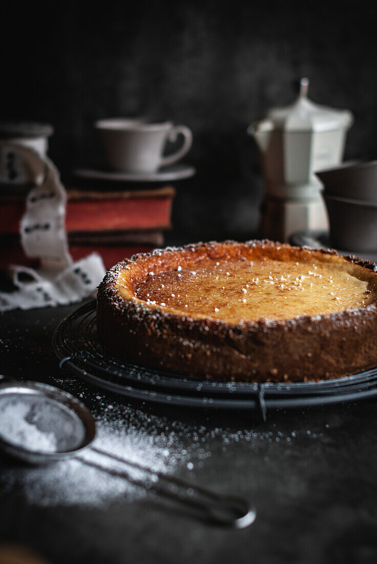 From above of tasty homemade aromatic cheesecake covered with powdered sugar placed on baking pan near cookware and strainer on black table