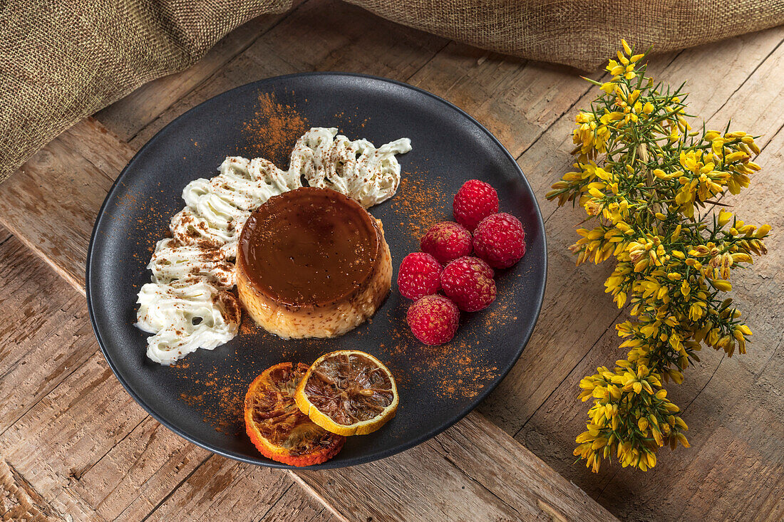 From above of tasty flan with whipped cream and red orange slices with cinnamon powder on ceramic plate