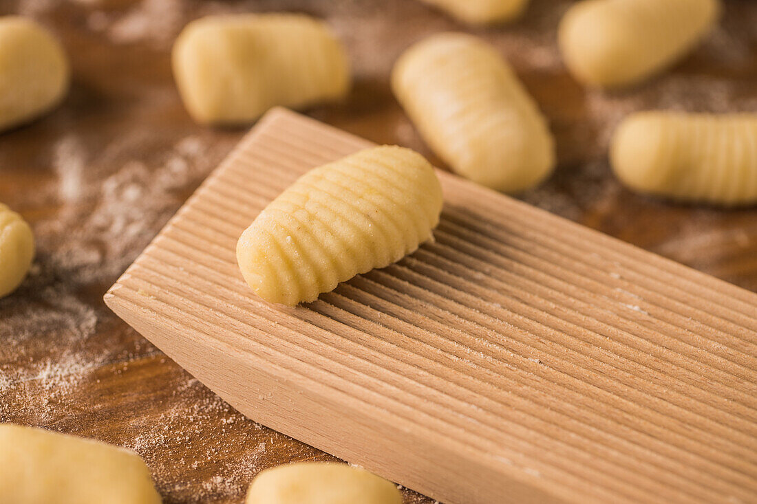 Top view of pieces of soft raw dough placed on wooden table covered with flour near ribber board during gnocchi preparation in the kitchen