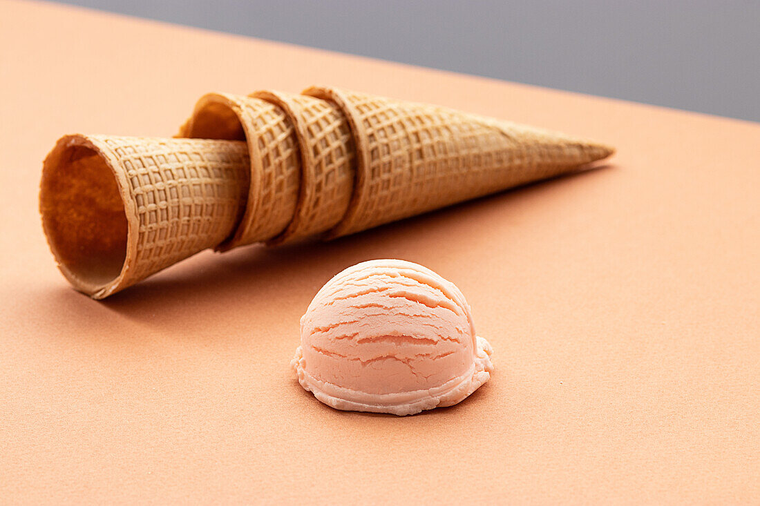 Pink ice cream scoop and waffle cones placed on table in studio