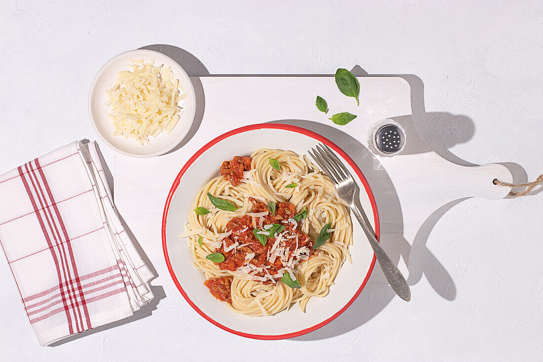Draufsicht auf einen Teller mit Spaghetti Bolognese mit Tomatensauce auf weißem Tischhintergrund