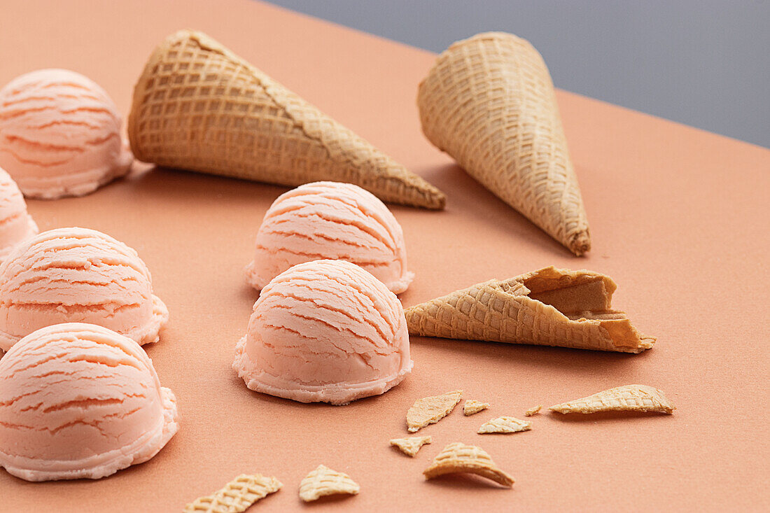 Pink ice cream scoop and waffle cones placed on table in studio