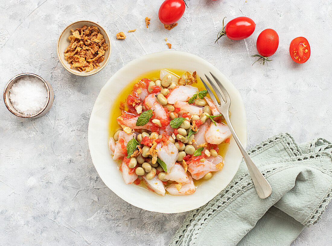 Tomaten- und Kabeljausalat mit reichlich Olivenöl in einem tiefen Teller mit einer Gabel und einer Schale mit gebratenen Zwiebeln