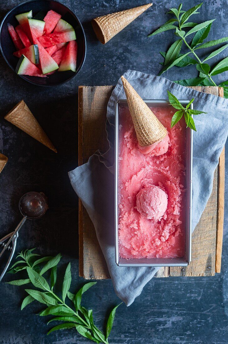 Von oben in einem Metallbehälter mit köstlichem Wassermelonensorbet auf einer grauen Serviette und einem Tisch an einem Sommertag platziertes Kornett