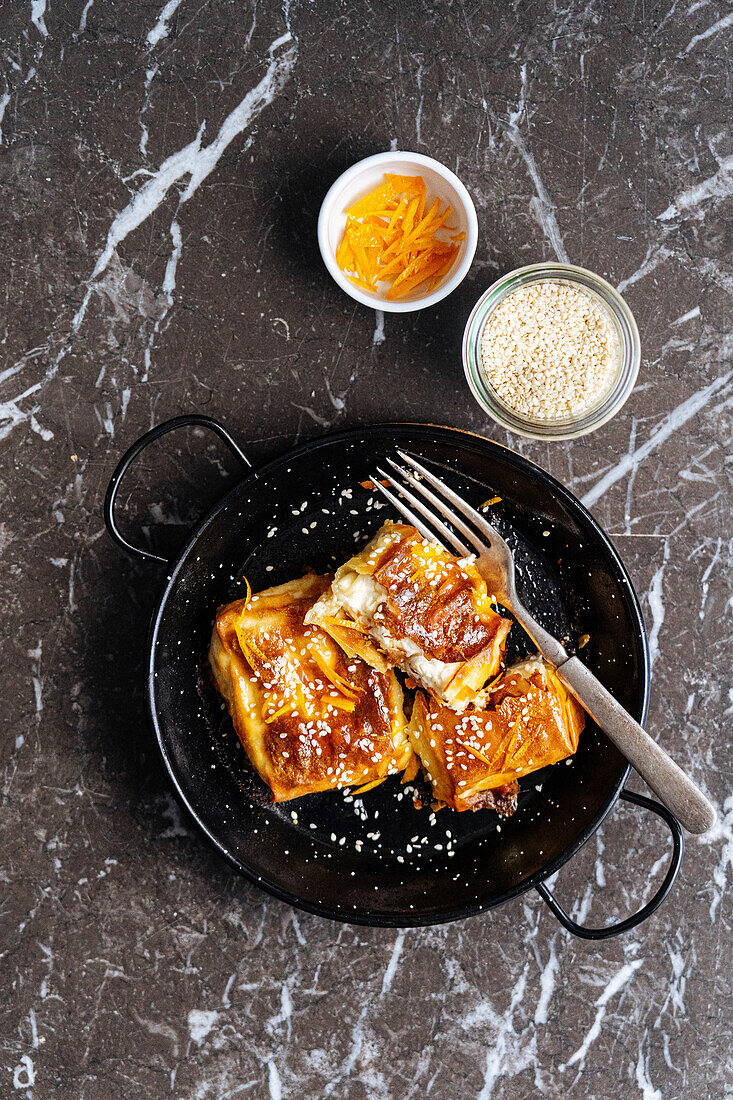 Top view of sweet tasty pastry with sesame seeds served on black plate with fork in light kitchen