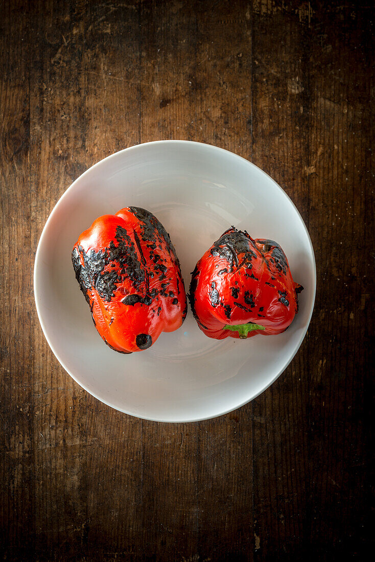 Top view of delicious whole grilled red peppers in round shaped ceramic bowl on brown background