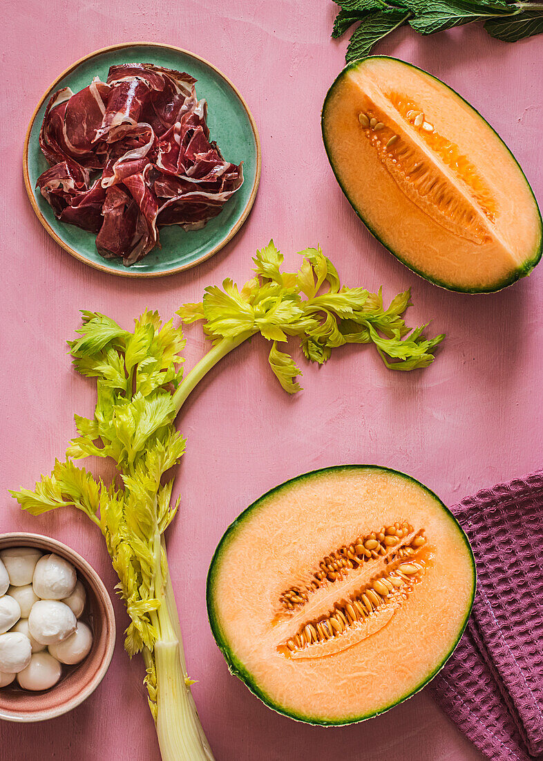 From above exotic melon, mozzarella and prosciutto ingredients for salad preparation on pink colorful background