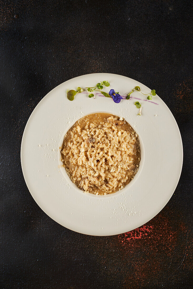 Blick von oben auf köstliches Porchini-Pilz-Risotto, serviert auf Teller mit Sprossen und Blume auf dunklem Hintergrund