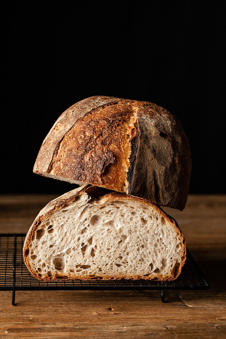 Halves of tasty sourdough bread with brown crust placed on grill tray on wooden table against black backdrop