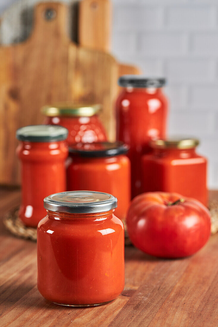 Sealed glass jar with handmade tomato sauce placed on table in kitchen at home