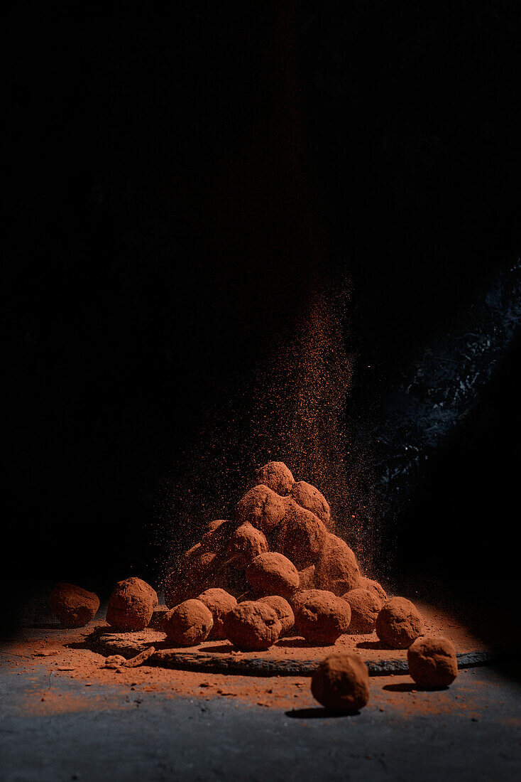 Heap of delicious chocolate truffles in shape of balls stacked on table on dark background in studio
