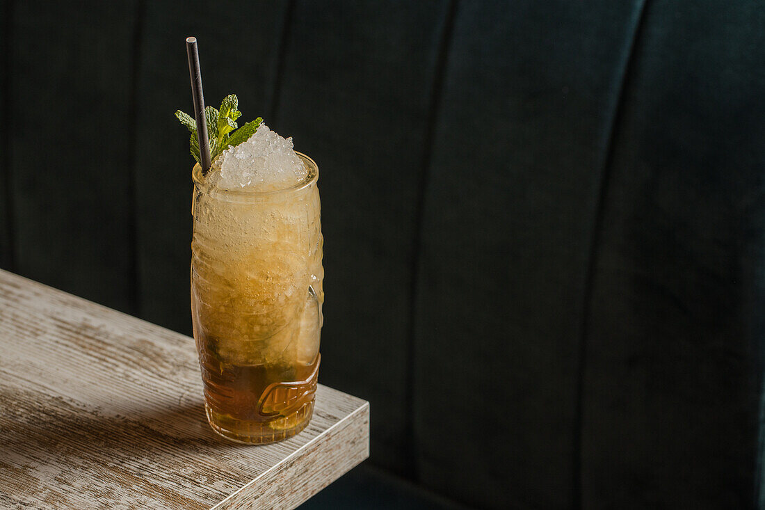 From above of tiki cup with cold alcohol drink with straw served with ice and decorated with fresh herb placed on blurred background