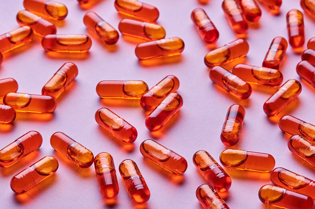 Top view composition of orange pills scattered on pink background in light studio