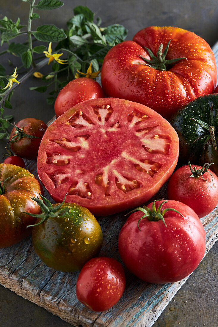 High angle of sliced tomato with salt placed on wooden chopping board among ripe red tomatoes with water drops