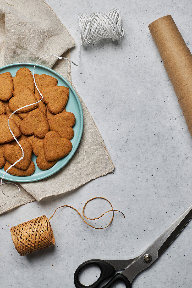 Top view of layout of sweet heart shaped Christmas biscuits on plate and assorted wrapping materials on table