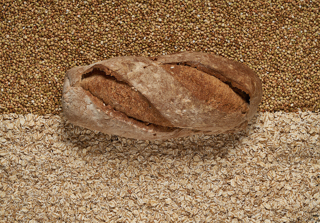 Top view full frame of fresh healthy brown baked bread placed on raw buckwheat and oat grains in light room