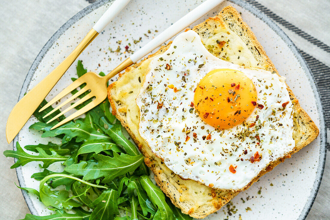 From above toast with eggs and cheese and rocket lettuce served on plate on table background